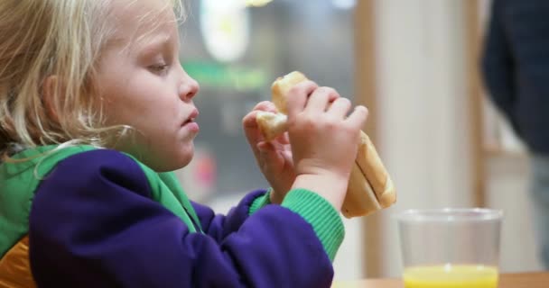 Little Blonde Girl Bright Warm Jacket Eats Sandwich Sitting Cafe — стоковое видео