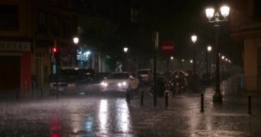 VALENCIA, SPAIN - JULY 13, 2022: Car under the rain at night. Vehicle with lit headlights moving along the wet city street with bright lantern