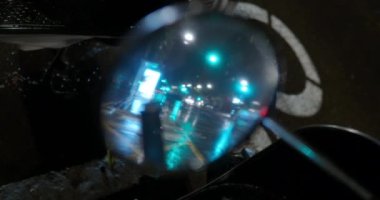 Dikiz aynasından yansıyan araba trafiği. Geceleri yağmurlu hava, ıslak yol ve yeşil trafik ışıkları
