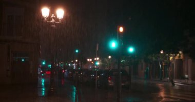 Night city view with heavy rain pouring and lightning flashing. Lit lanterns, blinking traffic lights and unidentified man soaking in dark street