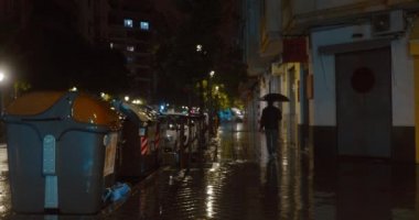 Issız caddede yürüyen şemsiyeli bir adam. Gece kentinde sağanak yağmur