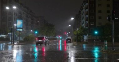 Trafik ışıkları yansımalı ıslak sokaklar ve az sayıda araba sürüyor. Geceleri yağmur yağar şehirde.