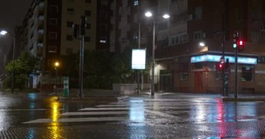 Geceleri yağmurun altında şehir manzarası. Islak cadde boyunca yeşil ışıklarda giden birkaç araba ve apartman dairesi.