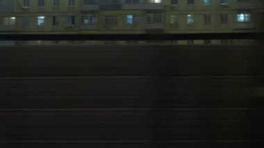 Akşamları hareket halindeki trenin camından dışarı bakıyorum. Metal çitin arkasındaki apartman bloklarının yanından geçiyorum.