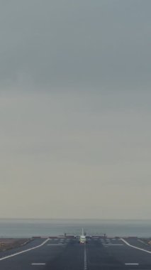 Vertical video, front view - a passenger plane with the side lights and headlights on, taxis to the runway and takes off
