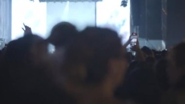 Audience dancing with hands up at the concert. Crowd of young people is excited with music and stage performance