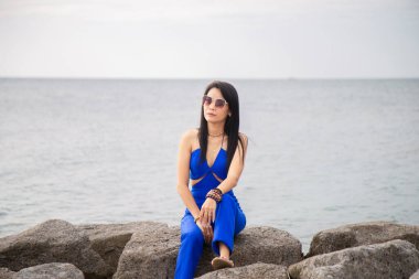 Asya 'da seyahat ederken deniz üzerindeki uçurumda oturan mavi gözlüklü Asyalı kadın portresi.