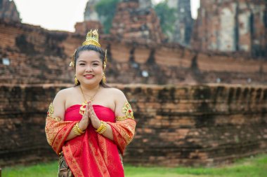 Tayland elbisesi giymiş gülümseyen Asyalı kadının portresi eski bir pagoda geçmişiyle saygılarını sunuyor.