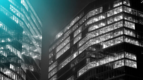 Corporate building at night - business concept. Glass wall office building .Modern office windows of skyscraper glowing at night. Black amd white.