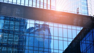 Gökyüzü arka planında cam cepheli modern ofis binası. Ofis binasının şeffaf cam duvarı ve güneş ışığı.