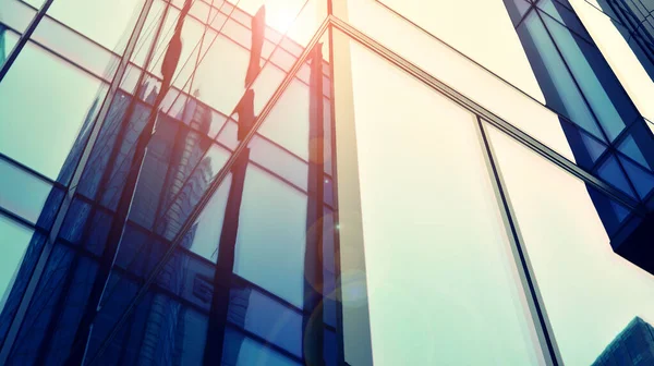 Gökyüzü arka planında cam cepheli modern ofis binası. Ofis binasının şeffaf cam duvarı ve güneş ışığı.