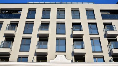 Güneşli bir günde modern bir apartman dairesi cephesi. Kocaman pencereleri ve balkonları olan modern apartmanlar..