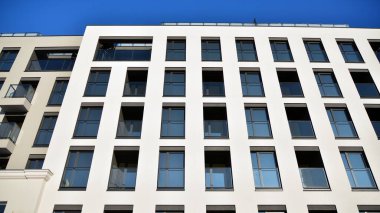 Güneşli bir günde modern bir apartman dairesi cephesi. Kocaman pencereleri ve balkonları olan modern apartmanlar..