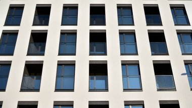 Güneşli bir günde modern bir apartman dairesi cephesi. Kocaman pencereleri ve balkonları olan modern apartmanlar..