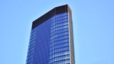 Ticari bina mavi tonda kapanıyor. Aşağıdan devasa bir gökdelen. Modern bina ve cam cephesinin mimari detayları. Güneşli bir günde iş geçmişi. 
