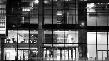 İnanılmaz bir gece manzarası. Geceleri ofis binası, cam ve ışıklarla bina cephesi. Aydınlatılmış modern gökdelen manzarası. Akşamları gökdelenlerin parlayan manzaralı pencereleri. Siyah ve beyaz.