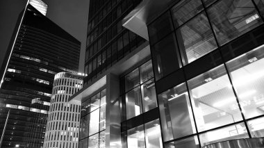 İnanılmaz bir gece manzarası. Geceleri ofis binası, cam ve ışıklarla bina cephesi. Aydınlatılmış modern gökdelen manzarası. Akşamları gökdelenlerin parlayan manzaralı pencereleri. Siyah ve beyaz.