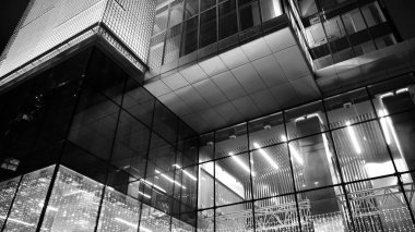 İnanılmaz bir gece manzarası. Geceleri ofis binası, cam ve ışıklarla bina cephesi. Aydınlatılmış modern gökdelen manzarası. Akşamları gökdelenlerin parlayan manzaralı pencereleri. Siyah ve beyaz.