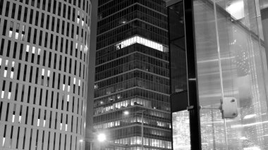 İnanılmaz bir gece manzarası. Geceleri ofis binası, cam ve ışıklarla bina cephesi. Aydınlatılmış modern gökdelen manzarası. Akşamları gökdelenlerin parlayan manzaralı pencereleri. Siyah ve beyaz.