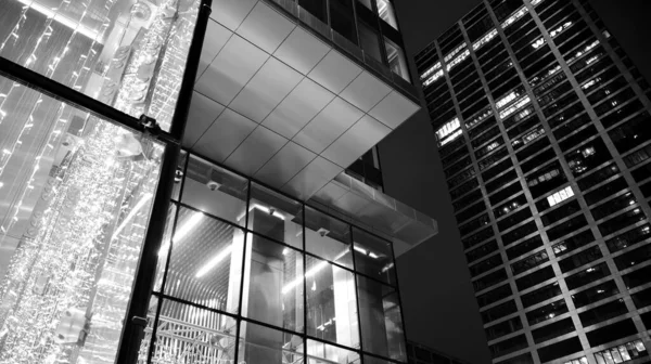 İnanılmaz bir gece manzarası. Geceleri ofis binası, cam ve ışıklarla bina cephesi. Aydınlatılmış modern gökdelen manzarası. Akşamları gökdelenlerin parlayan manzaralı pencereleri. Siyah ve beyaz.