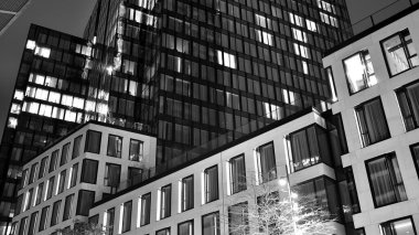 İnanılmaz bir gece manzarası. Geceleri ofis binası, cam ve ışıklarla bina cephesi. Aydınlatılmış modern gökdelen manzarası. Akşamları gökdelenlerin parlayan manzaralı pencereleri. Siyah ve beyaz.