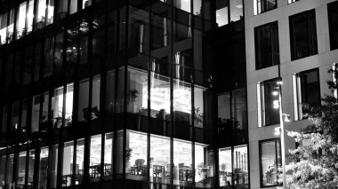 İnanılmaz bir gece manzarası. Geceleri ofis binası, cam ve ışıklarla bina cephesi. Aydınlatılmış modern gökdelen manzarası. Akşamları gökdelenlerin parlayan manzaralı pencereleri. Siyah ve beyaz.