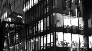 İnanılmaz bir gece manzarası. Geceleri ofis binası, cam ve ışıklarla bina cephesi. Aydınlatılmış modern gökdelen manzarası. Akşamları gökdelenlerin parlayan manzaralı pencereleri. Siyah ve beyaz.