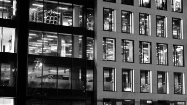 İnanılmaz bir gece manzarası. Geceleri ofis binası, cam ve ışıklarla bina cephesi. Aydınlatılmış modern gökdelen manzarası. Akşamları gökdelenlerin parlayan manzaralı pencereleri. Siyah ve beyaz.
