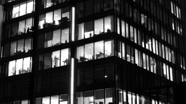 İnanılmaz bir gece manzarası. Geceleri ofis binası, cam ve ışıklarla bina cephesi. Aydınlatılmış modern gökdelen manzarası. Akşamları gökdelenlerin parlayan manzaralı pencereleri. Siyah ve beyaz.