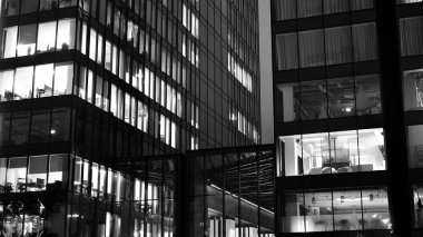 İnanılmaz bir gece manzarası. Geceleri ofis binası, cam ve ışıklarla bina cephesi. Aydınlatılmış modern gökdelen manzarası. Akşamları gökdelenlerin parlayan manzaralı pencereleri. Siyah ve beyaz.