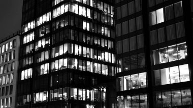 İnanılmaz bir gece manzarası. Geceleri ofis binası, cam ve ışıklarla bina cephesi. Aydınlatılmış modern gökdelen manzarası. Akşamları gökdelenlerin parlayan manzaralı pencereleri. Siyah ve beyaz.