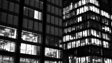 İnanılmaz bir gece manzarası. Geceleri ofis binası, cam ve ışıklarla bina cephesi. Aydınlatılmış modern gökdelen manzarası. Akşamları gökdelenlerin parlayan manzaralı pencereleri. Siyah ve beyaz.