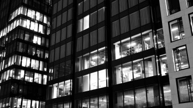 İnanılmaz bir gece manzarası. Geceleri ofis binası, cam ve ışıklarla bina cephesi. Aydınlatılmış modern gökdelen manzarası. Akşamları gökdelenlerin parlayan manzaralı pencereleri. Siyah ve beyaz.