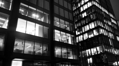 İnanılmaz bir gece manzarası. Geceleri ofis binası, cam ve ışıklarla bina cephesi. Aydınlatılmış modern gökdelen manzarası. Akşamları gökdelenlerin parlayan manzaralı pencereleri. Siyah ve beyaz.
