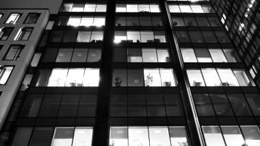 İnanılmaz bir gece manzarası. Geceleri ofis binası, cam ve ışıklarla bina cephesi. Aydınlatılmış modern gökdelen manzarası. Akşamları gökdelenlerin parlayan manzaralı pencereleri. Siyah ve beyaz.