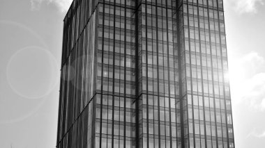 Şehir merkezindeki soyut ve karmaşık gökdelen yapısının arka planında gökyüzü ve güneş var. Siyah ve beyaz.