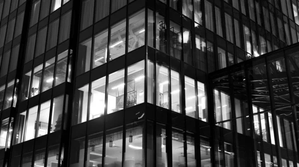 İnanılmaz bir gece manzarası. Geceleri ofis binası, cam ve ışıklarla bina cephesi. Aydınlatılmış modern gökdelen manzarası. Akşamları gökdelenlerin parlayan manzaralı pencereleri. Siyah ve beyaz.