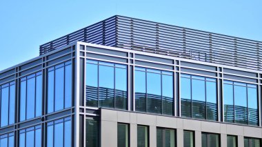 Minimalist cam cephe, büyük şeffaf panelleri tutan çelik iskelet. Çağdaş ticari mimari, dikey geometrik çizgiler. Cam panellerde mavi gökyüzü yansıması