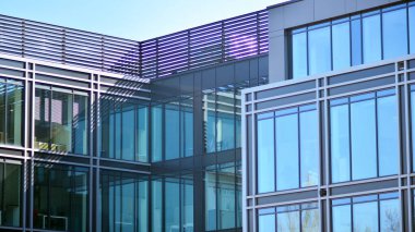 Minimalist cam cephe, büyük şeffaf panelleri tutan çelik iskelet. Çağdaş ticari mimari, dikey geometrik çizgiler. Cam panellerde mavi gökyüzü yansıması