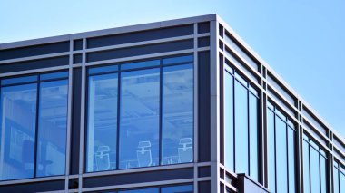 Minimalist cam cephe, büyük şeffaf panelleri tutan çelik iskelet. Çağdaş ticari mimari, dikey geometrik çizgiler. Cam panellerde mavi gökyüzü yansıması