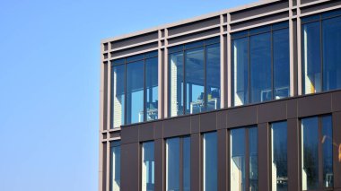 Minimalist cam cephe, büyük şeffaf panelleri tutan çelik iskelet. Çağdaş ticari mimari, dikey geometrik çizgiler. Cam panellerde mavi gökyüzü yansıması