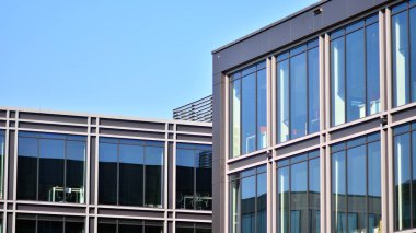 Minimalist cam cephe, büyük şeffaf panelleri tutan çelik iskelet. Çağdaş ticari mimari, dikey geometrik çizgiler. Cam panellerde mavi gökyüzü yansıması