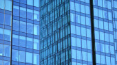 Skleněná budova s průsvitnou fasádou budovy a modrou oblohou. Strukturální skleněná stěna odrážející modré nebe. Abstraktní fragment moderní architektury. Současné architektonické pozadí.