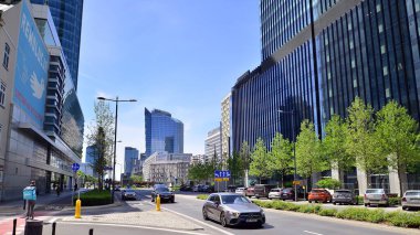Varşova, Polonya. 16 Mayıs 2022. Mavi gökyüzüne karşı cam gökdelenler ve şehir merkezinde trafik. Binaların mimarisi ve caddelerde arabaları olan renkli şehir manzarası. Şehirde hava güneşli..