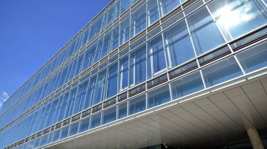 Mavi gökyüzüne karşı modern cam cephe. İş bölgesindeki bir binanın alt manzarası. Bir ofis binasının cam cephesinin alçak açılı görüntüsü.