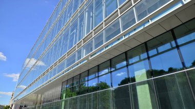 Mavi gökyüzüne karşı modern cam cephe. İş bölgesindeki bir binanın alt manzarası. Bir ofis binasının cam cephesinin alçak açılı görüntüsü.