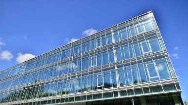 Mavi gökyüzüne karşı modern cam cephe. İş bölgesindeki bir binanın alt manzarası. Bir ofis binasının cam cephesinin alçak açılı görüntüsü.