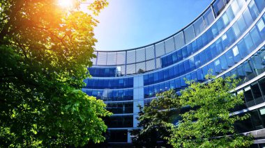 Gökyüzü arka planında cam cepheli modern ofis binası. Ofis binasının şeffaf cam duvarı. Mavi gökyüzünde güneşli, güneşli bir gün. Velvia grafik filtresi.