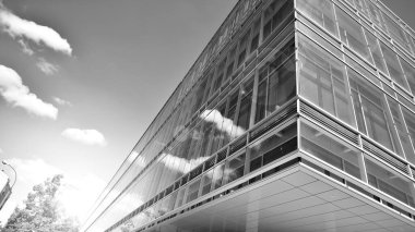 Gökyüzü arka planında cam cepheli modern ofis binası. Ofis binasının şeffaf cam duvarı. Gökyüzünde güneş ışığı olan güneşli bir gün. Siyah ve beyaz.