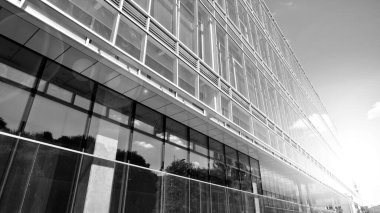 Gökyüzü arka planında cam cepheli modern ofis binası. Ofis binasının şeffaf cam duvarı. Gökyüzünde güneş ışığı olan güneşli bir gün. Siyah ve beyaz.